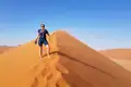 Eine Person steht oben auf einer Sanddüne und signalisiert Erfolg.