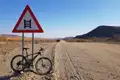 Fahrrad an einem Viehgitter-Warnschild auf einer Schotterpiste.