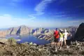 Drei Personen stehen auf einem Berg und blicken auf eine Bucht und die umliegenden Berge.