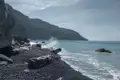 Wellen, die auf einen Kieselstrand treffen, mit einer Bergkette im Hintergrund.