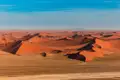 Ausgedehnte rote Sanddünenlandschaft unter blauem Himmel.