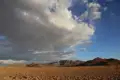 Regenbogen über einer Wüstenlandschaft mit Bergen im Hintergrund.