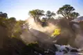 Sonnenaufgang über einem Wasserfall mit Baobab Bäumen im Vordergrund.