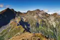 Felsige Berggipfel und grüne Täler unter blauem Himmel.
