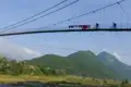 Zwei Radfahrer auf einer Hängebrücke mit Bergen im Hintergrund.