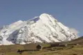Schneebedeckter Berggipfel in den Anden mit einer kleinen Hütte und Steinmauern im Vordergrund.