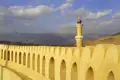 Festungsmauer mit Minarett und Berglandschaft im Hintergrund.