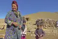 Eine Frau mit zwei Kindern vor traditionellen Steinhütten in einer bergigen Landschaft.