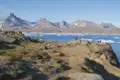 Campingplatz in einer arktischen Landschaft mit Zelten, Eisbergen und Bergen im Hintergrund.