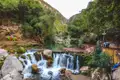Ein Wasserfall in einer bewaldeten Schlucht mit Sitzgelegenheiten am Ufer.