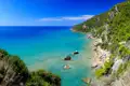 Türkisblaues Meer und Sandstrand an einer bewaldeten Küste.
