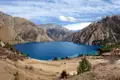 Panoramablick auf einen tiefblauen Bergsee, umgeben von einer kargen Landschaft und steilen Berghängen.