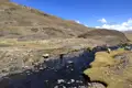 Berglandschaft mit Fluss und grasenden Schafen.