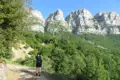 Wanderer mit Trekkingstöcken auf einem Pfad inmitten grüner Landschaft, im Hintergrund hohe, felsige Berge.