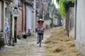 Person mit traditionellem Hut fährt Fahrrad durch Dorfgasse.