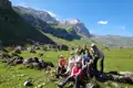 Wandergruppe pausiert im grünen Tal mit Blick auf einen schneebedeckten Berg.
