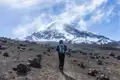 Wanderer auf einem felsigen Pfad mit Blick auf einen schneebedeckten Vulkan.