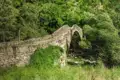 Historische Steinbrücke über einen Fluss inmitten grüner Natur.