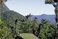Terrassierte Anlage im tropischen Regenwald, umgeben von Palmen und bewaldeten Bergen.