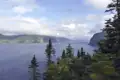 Panoramablick auf einen Fjord, umgeben von bewaldeten Hügeln und felsigen Klippen.