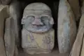 Antike Statue mit Bemalung und Verzierungen, gefunden in einer steinernen Umgebung.