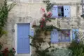 Lila Tür und Fensterläden an einem Steinhaus, umrankt von blühender Bougainvillea.