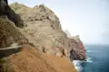 Schmaler Küstenpfad an steilen Klippen mit Blick auf das Meer.