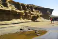 Wanderer erkunden eine Landschaft mit erodierten Felsformationen und einem kleinen Wasserlauf, der durch die Erosion entstanden ist.