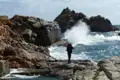 Wanderer fotografiert Brandung an felsiger Küste.