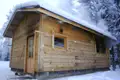 Eine verschneite Holzhütte mit aufsteigendem Rauch, der auf eine Wärmequelle im Inneren hindeutet.