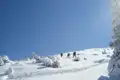 Drei Wanderer besteigen einen schneebedeckten Hang.