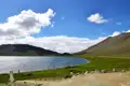 Panoramablick auf einen Bergsee mit umliegenden Bergen und grünem Ufer.