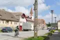 Traditionelle Häuser und Kirche in einem Dorf mit Storchennestern auf Strommasten.
