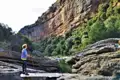 Wanderer in einer Schlucht mit Fluss und hohen Felswänden.