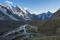 Basislager der Reise in einer hochalpinen Umgebung. Zelte stehen am Ufer eines sich verzweigenden Flusses, umgeben von schneebedeckten Gipfeln.