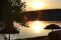 Sonnenuntergang über einem See, gesehen von einem Ufer mit Sonnenschirmen.