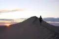 Silhouetten von Wanderern auf einer Sanddüne im Abendlicht.