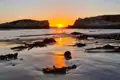 Sonnenuntergang zwischen Felsen am Strand mit Seetang im Vordergrund.