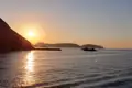 Sonnenuntergang über dem Meer mit Silhouette eines Bootes und Bergen.