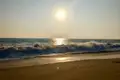Sonnenuntergang über dem Meer mit Wellen, die am Strand brechen.