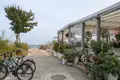 Strandrestaurant mit überdachter Terrasse und blühenden Blumen. Zwei Fahrräder stehen am Eingang. Ein Weg führt zum Strand.