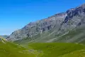 Grüne Hänge und felsige Gipfel eines Gebirges unter blauem Himmel.