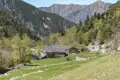 Traditionelles Steinhaus inmitten eines grünen Tals, umgeben von den bewaldeten Pyrenäen.