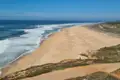 Panoramablick auf einen Sandstrand mit einlaufenden Wellen.
