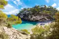 Ansicht einer malerischen Bucht mit klarem, türkisfarbenem Wasser und einem einladenden weißen Sandstrand, umgeben von üppigen grünen Pinien.