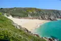 Türkisfarbenes Wasser und weißer Sandstrand umgeben von grünen Hügeln.
