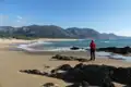 Person am Strand mit Blick auf Meer und Berge.