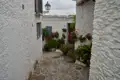 Schmale Gasse mit weiß getünchten Häusern und blühenden Blumen in Töpfen.