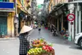 Straßenverkäuferin mit Strohhut und Fahrrad voller frischer Früchte in Hanoi.