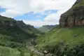 Grüne Hügellandschaft mit Flussbett und steilen Felswänden.
